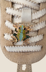Dettaglio della sneaker Madison Shop NOA in pelle beige con lacci bianchi e spilla decorativa a forma di rana