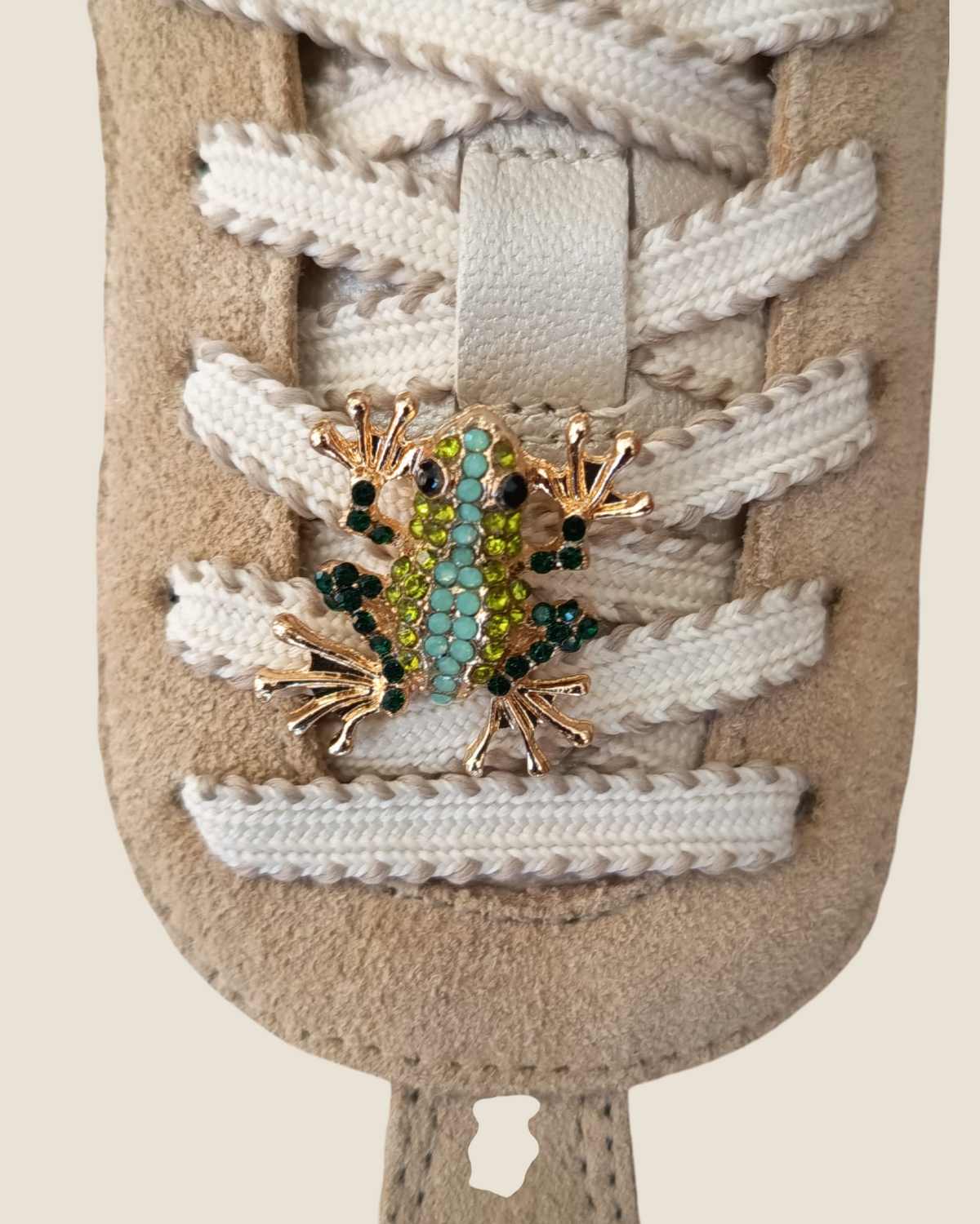 Dettaglio della sneaker Madison Shop NOA in pelle beige con lacci bianchi e spilla decorativa a forma di rana